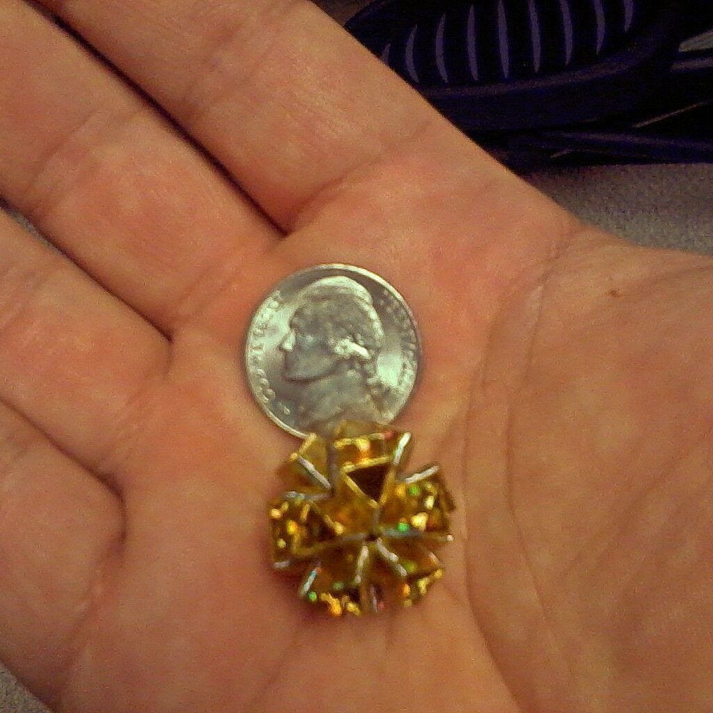 Icosahedron with 1/8 inch Ribbon open palm with head side of nickel and tiny nickel-sized gold wrapping paper origami