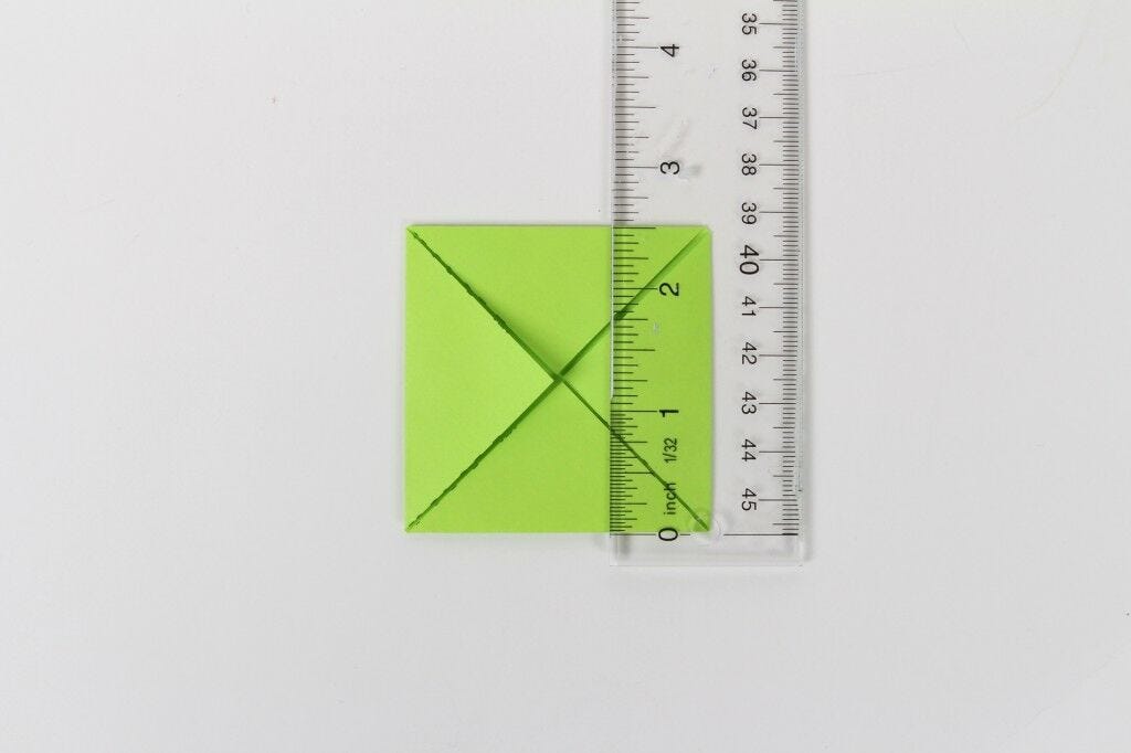 small green paper square origami folded in with clear measuring ruler