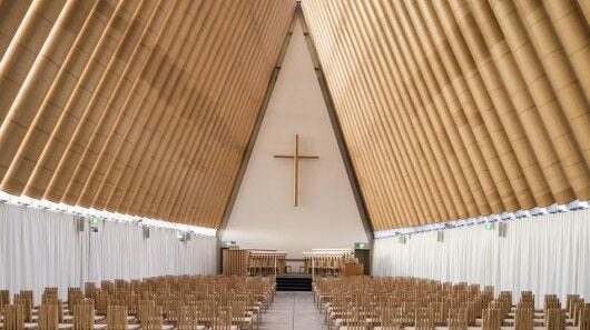 brown and white church interior with empty pews and cross on wall