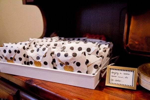 Cookies in white wrappings with black polka dots arranged on a shelf, a small framed sign next to it reading "enjoy a cookie favor now, or for later..."