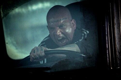 Rhino shouting with tattooed hand on steering wheel of car