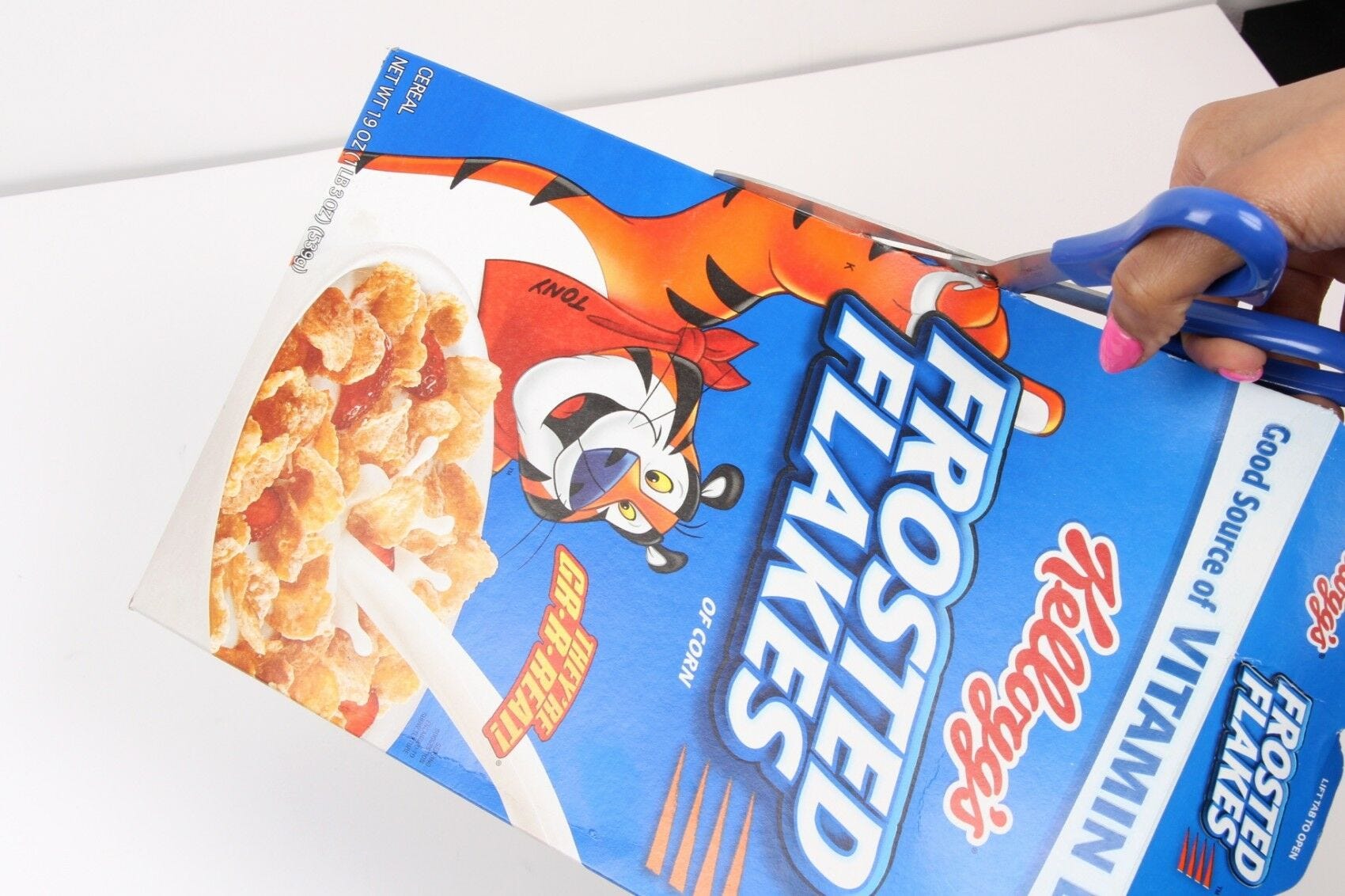 hand holding Frosted Flakes box and scissors