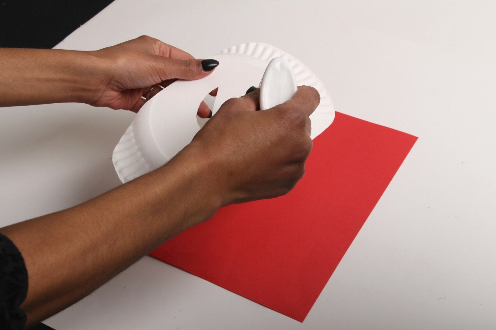 hands applying elmers glue to diy spiderman mask paper plate over red paper