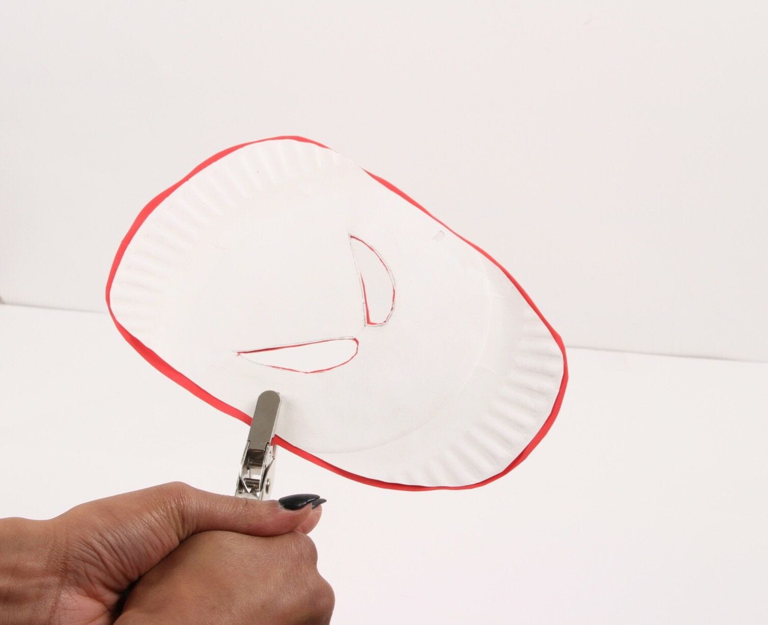 hands punching holes into paper mask with metal hole puncher