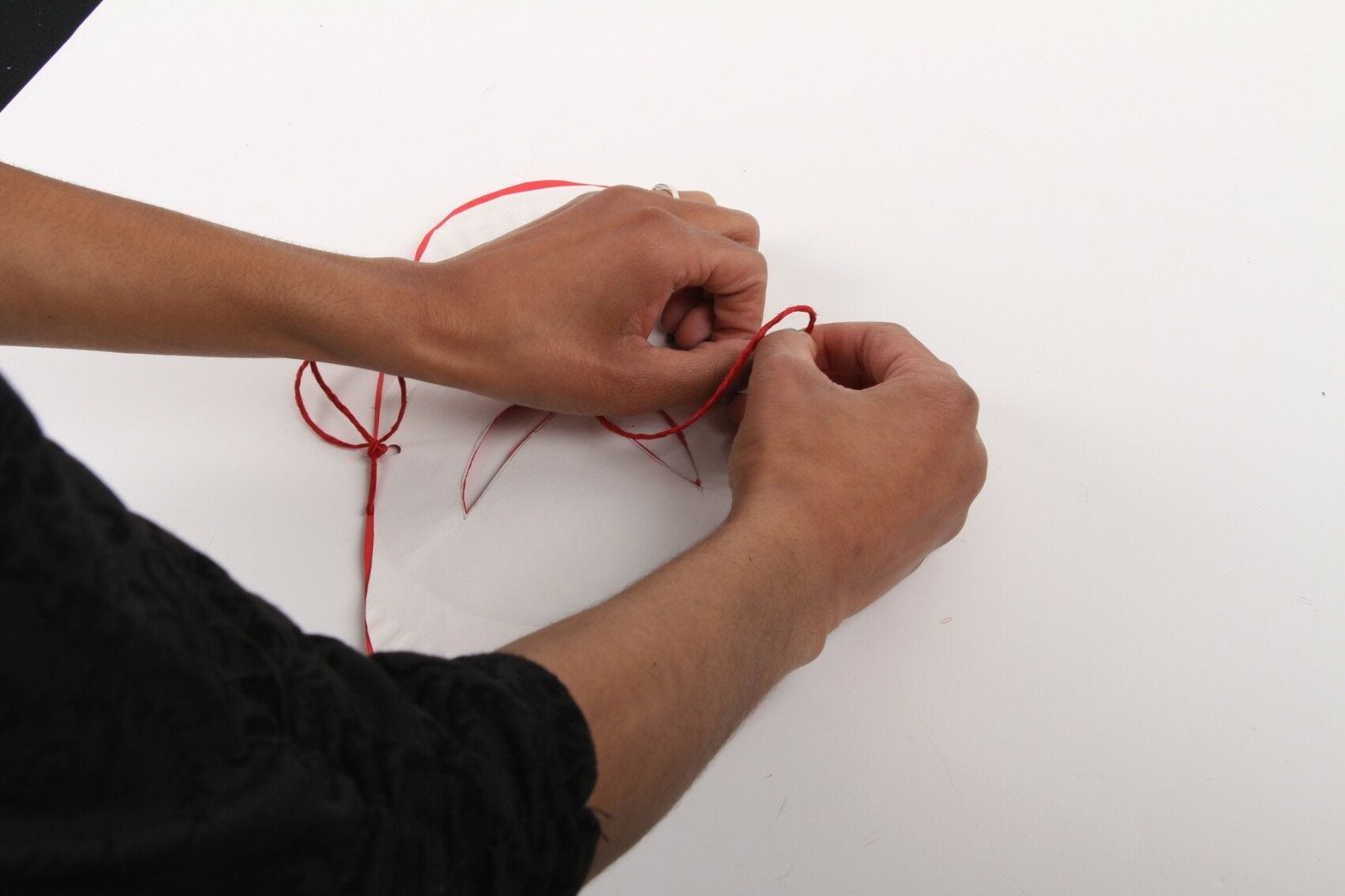 hands tying red string and knots on both sides of mask