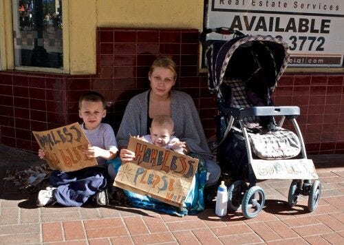 blonde woman and two children sitting on street holding homeless signs