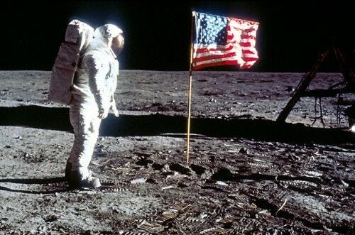 astronaut in space suit on moon with american flag in ground