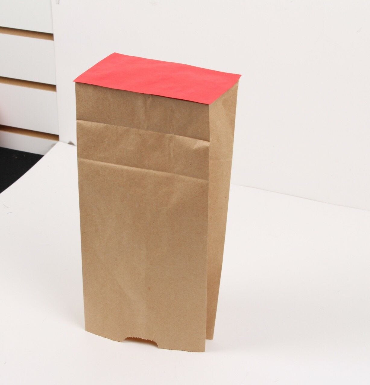 red paper rectangle pasted to bottom of brown paper bag