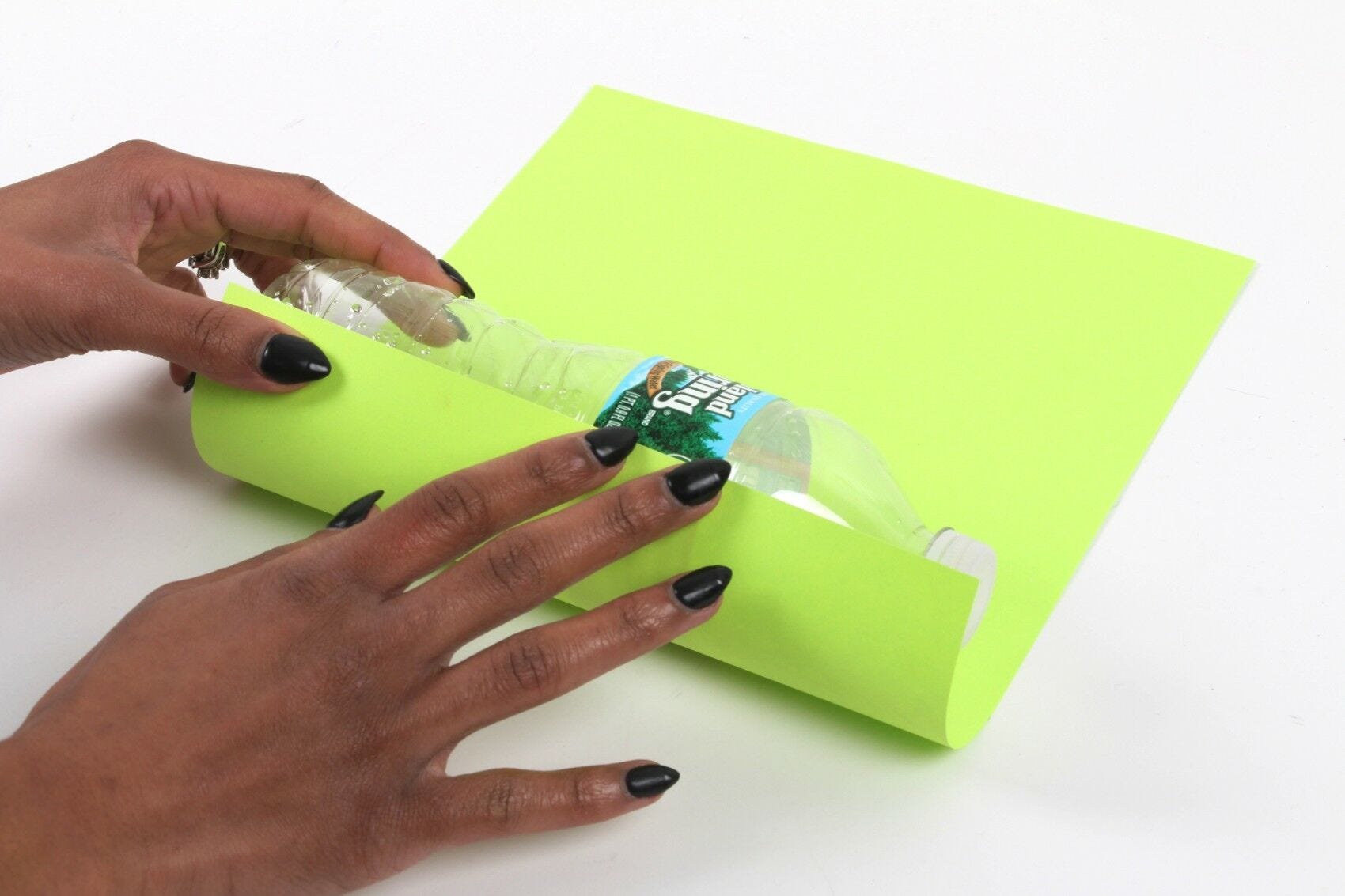 hands rolling empty plastic water bottle in lime green construction paper