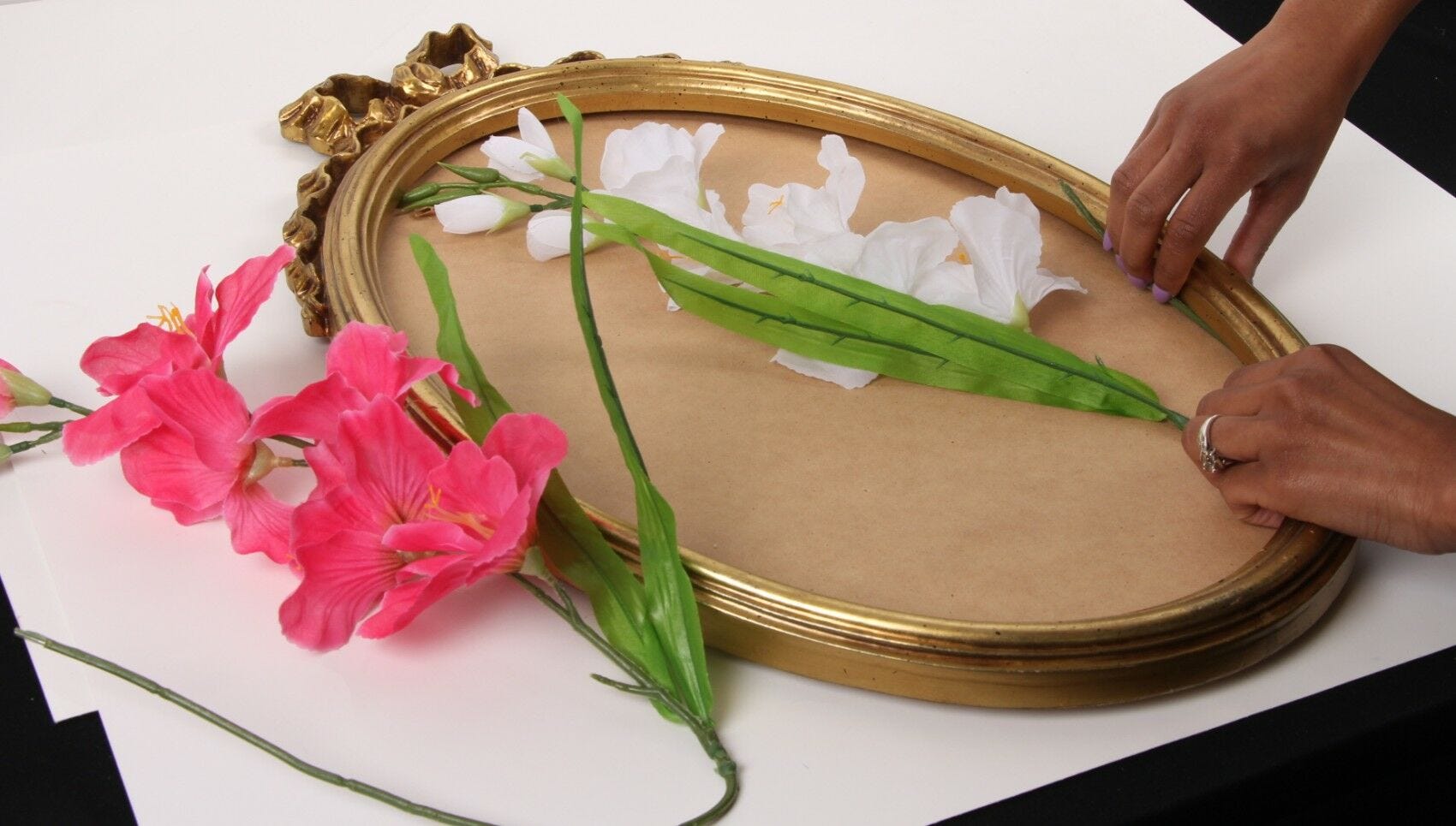 hands arranging pink and white silk flowers to mirror base