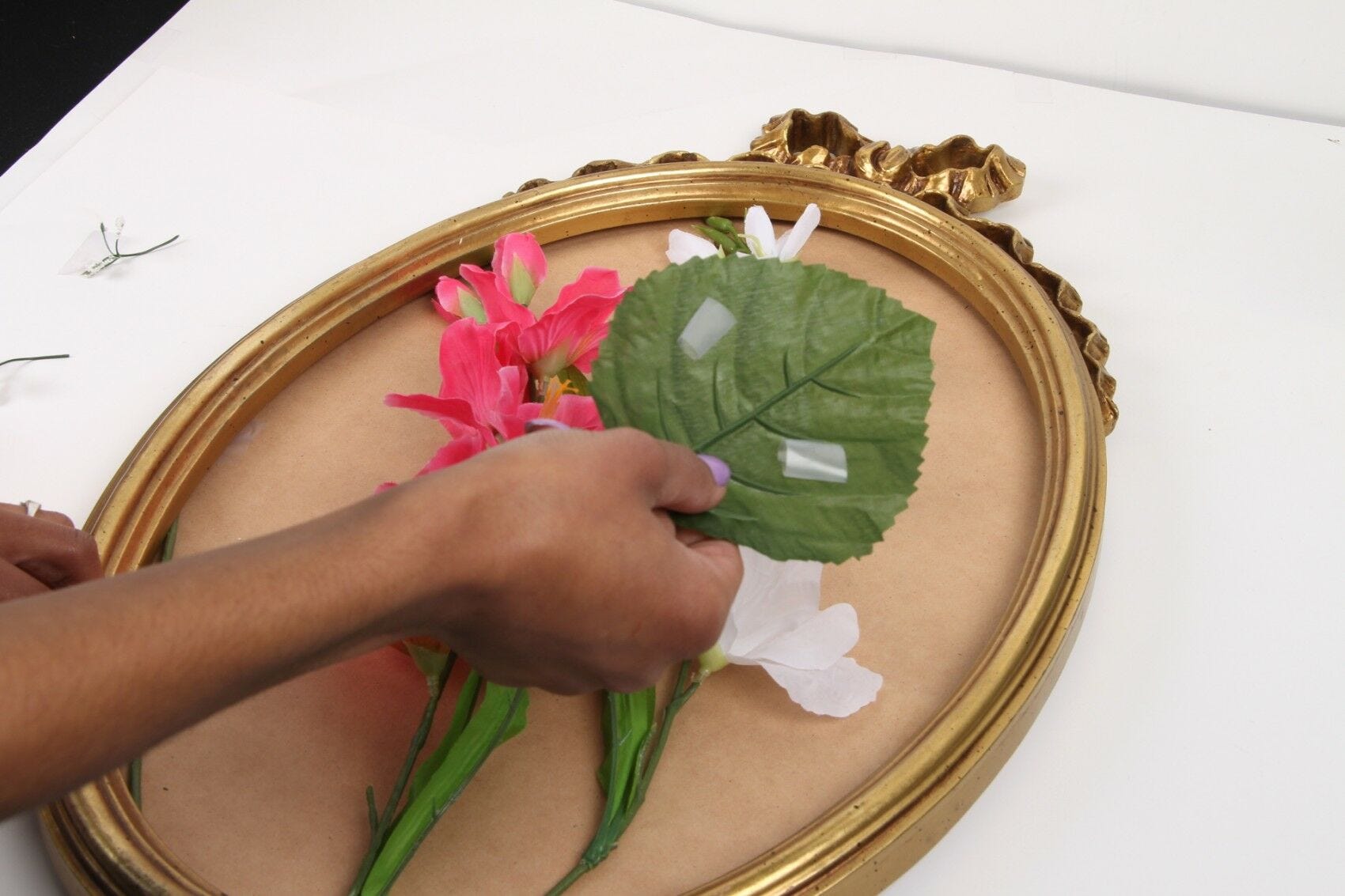 hands taping pink and white silk flowers and leaves to mirror base