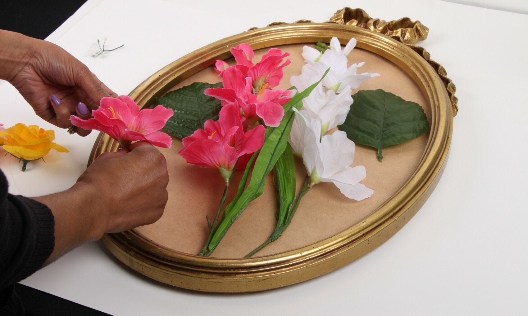 hands taping and attaching fake flowers to broken mirror