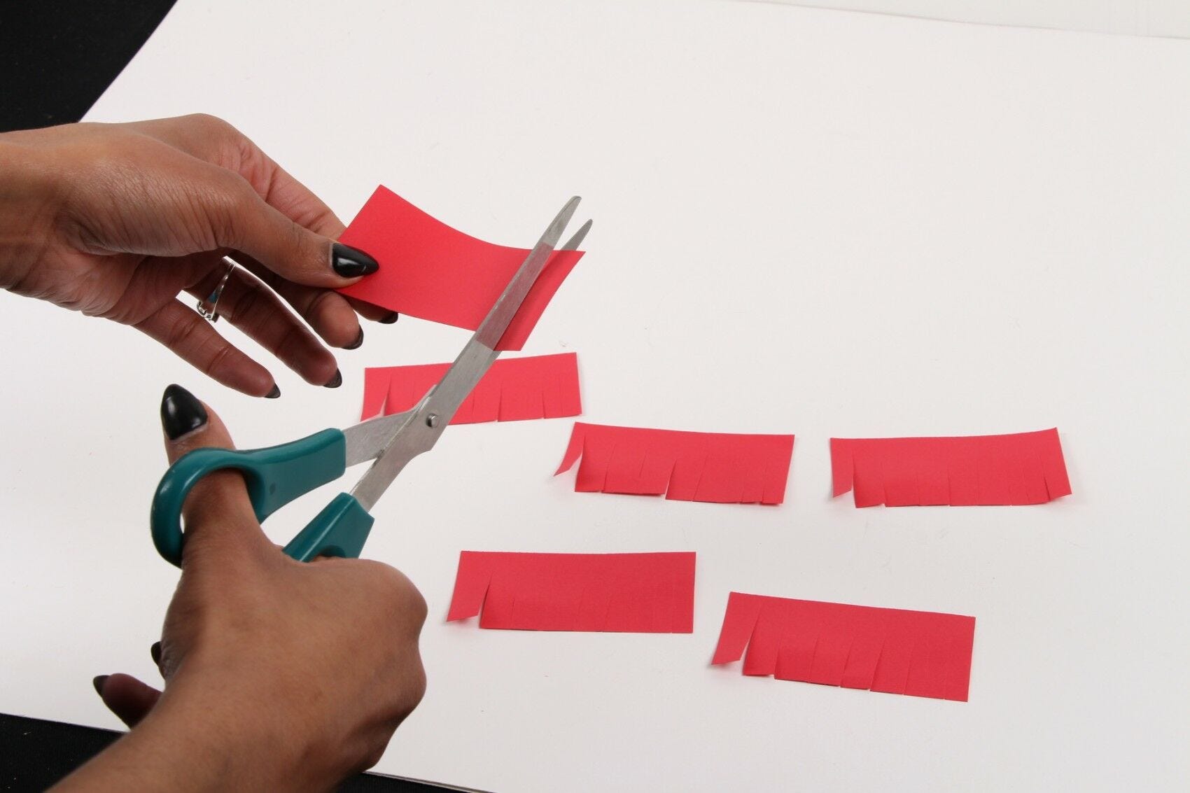 hands cutting fringe on red sticky notes with scissors