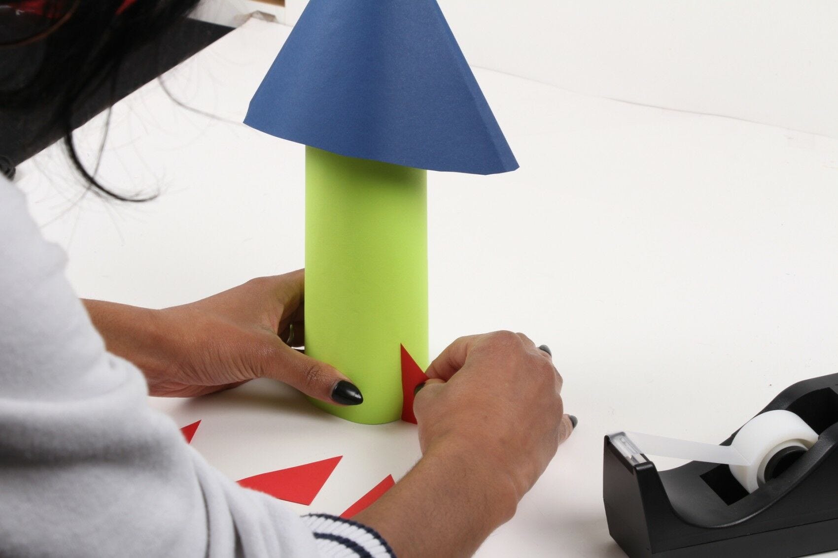 hands taping small red triangle to paper water bottle spaceship