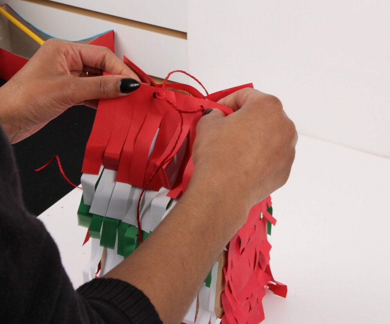 hands tying together red string threaded through top of paper bag