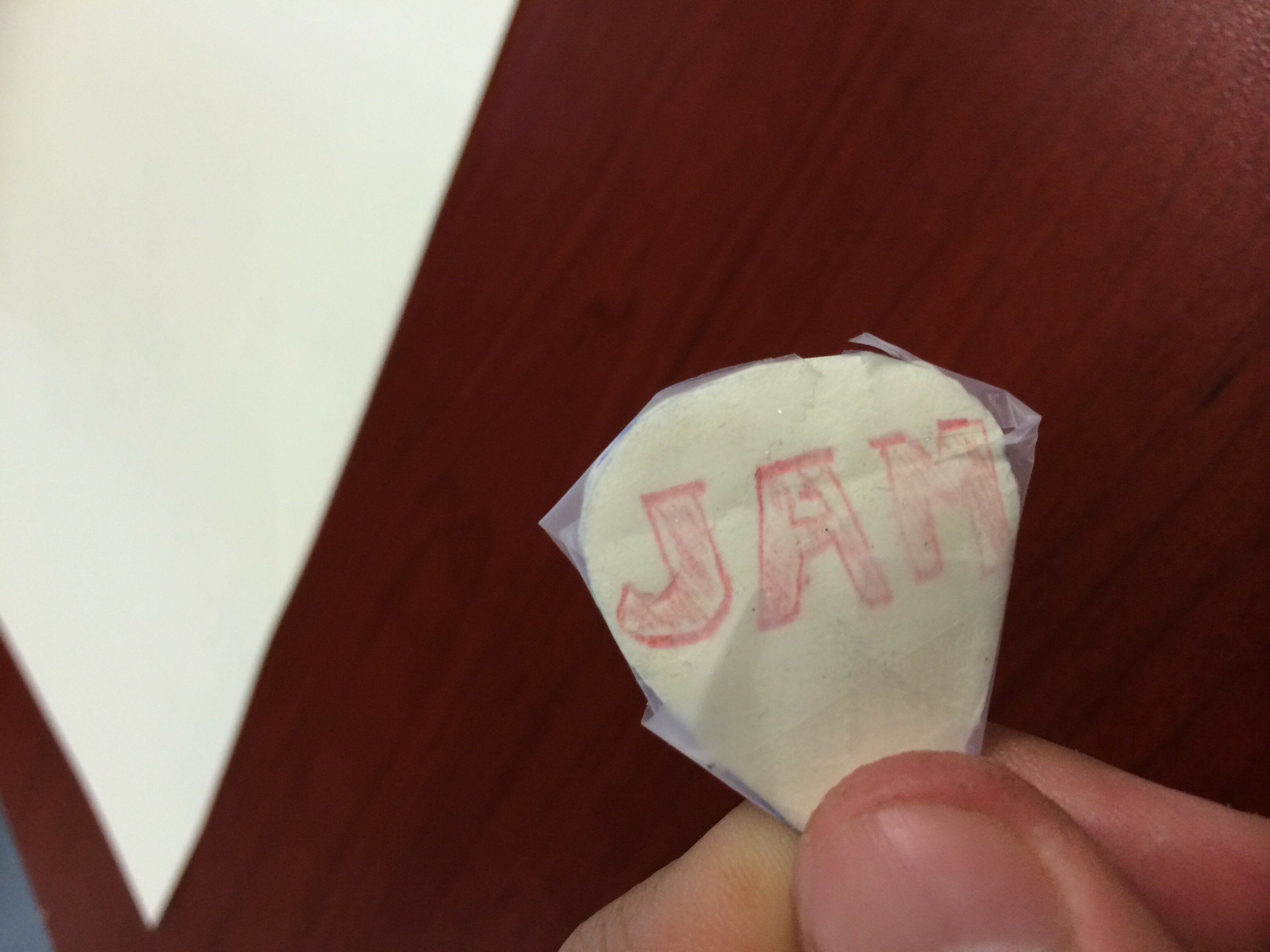 white paper cutout shape with red jam logo covered in scotch tape