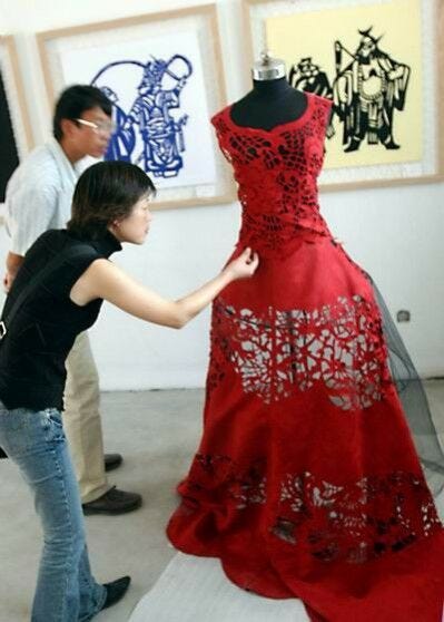 woman and man working on red papercut gown on mannequin