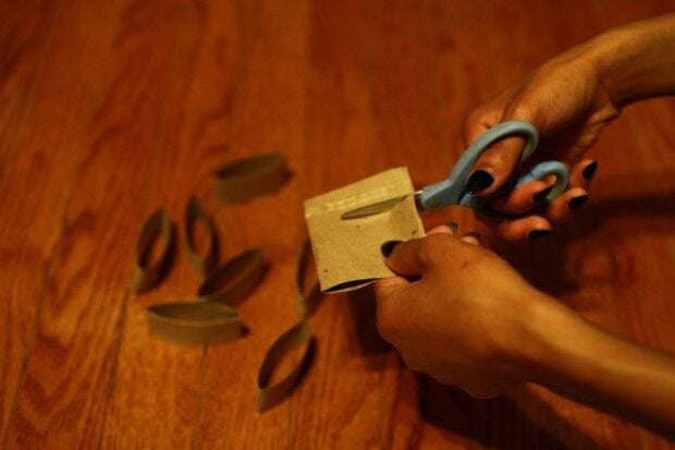 hands, paper towel tube, scissors cutting paper towel tube with scissors