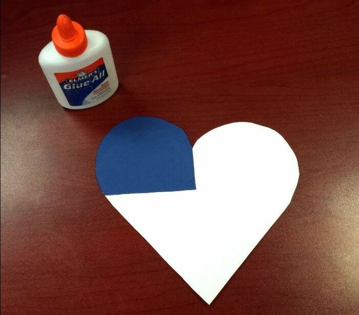 white paper heart on desk with blue paper in corner and glue bottle