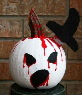 white pumpkin covered in red blood with black hilted knife sticking out of head