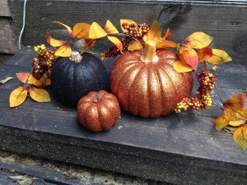 assortment of glittery orange and black pumpkins on black step with autumn leaf decor