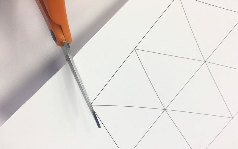 Using scissors to cut outer edge of triangle shapes on white paper