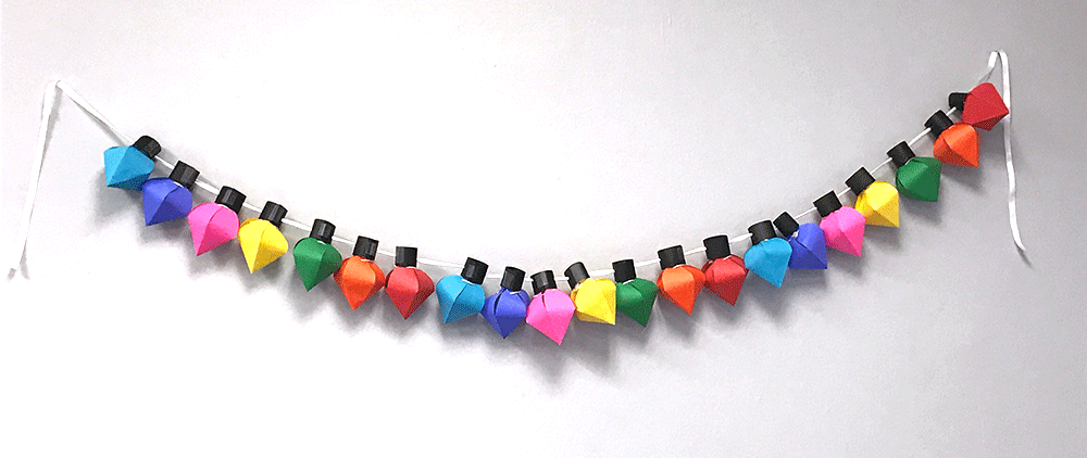 String of multi-colored card DIY card stock Christmas lights hung on white wall