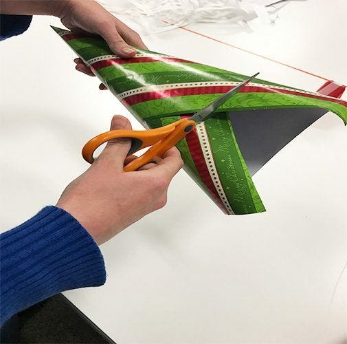 Cutting excess wrapping paper from cone with scissors