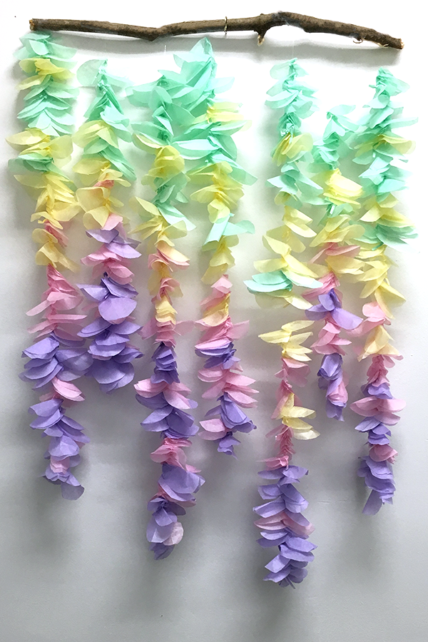 green yellow pink and purple tissue paper flower garland hanging from tree branch