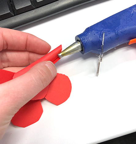 hand holding rolled flower petal and hot glue gun