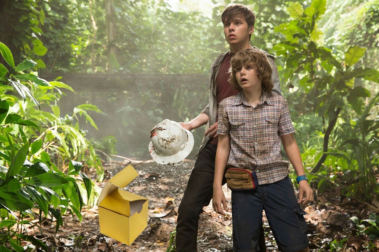 two boys standing in forest with open yellow cardboard box on ground