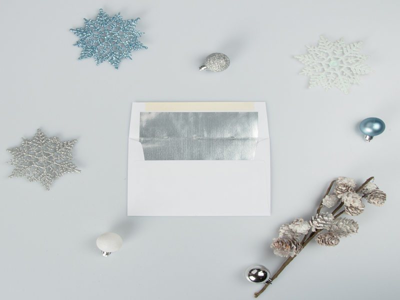 white and silver foil lined envelope with pinecones and blue white and silver ornaments and snowflakes