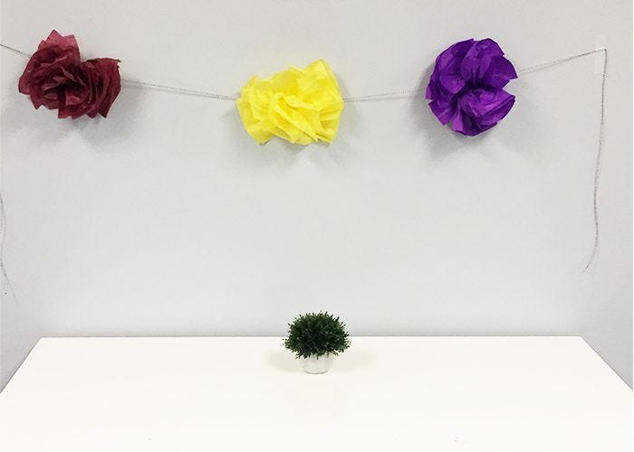 Yellow, burgundy, and purple pompom flowers strung from wall with twine