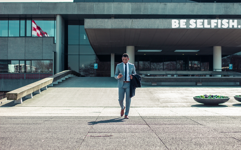 Man in a suit walking out of a building, caption "Be Selfish"