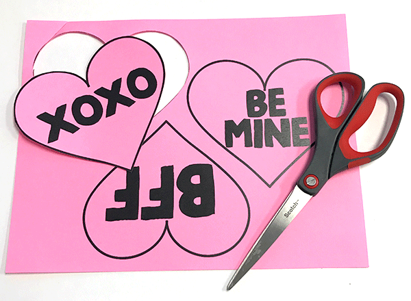 pair of scissors on top of pink cardstock with printed hearts and text template