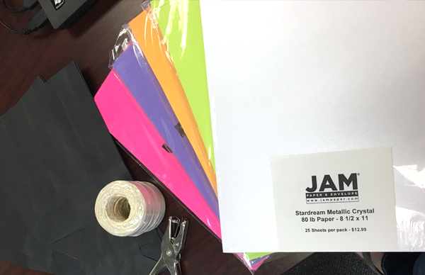 stacks of colored paper, spool of twine, and hole puncher spread on desk