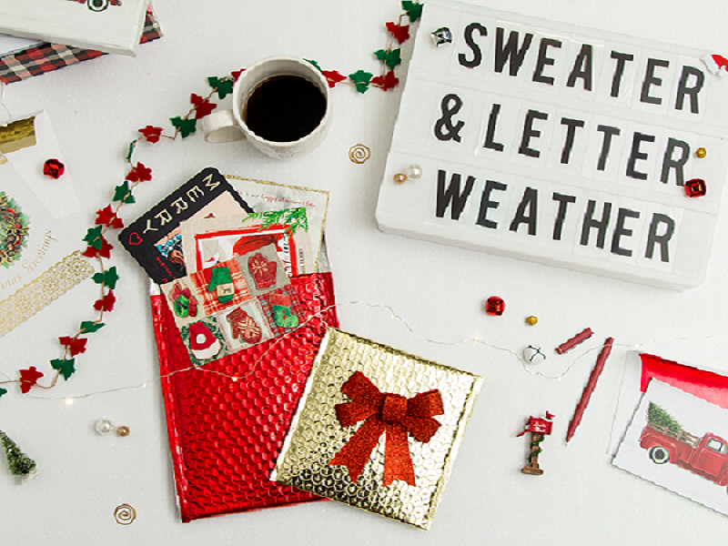 white desk layout with christmas decor and red and gold bubble mailers with christmas cards