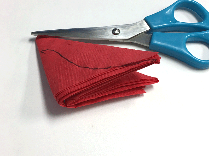 making diy paper cocktail napkin poinsettias: folded red napkin with black line and blue scissors